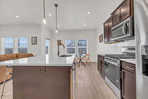 Kitchen featuring sink, appliances with stainless steel finishes, hanging light fixtures, dark brown cabinetry, and an island with sink