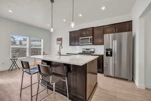 Kitchen with dark brown cabinets, appliances with stainless steel finishes, hanging light fixtures, and a center island with sink