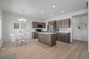 Kitchen with an island with sink, decorative light fixtures, black appliances, light hardwood / wood-style floors, and sink