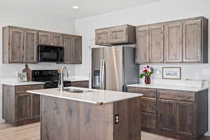 Kitchen featuring dark brown cabinetry, black appliances, light hardwood / wood-style floors, sink, and a kitchen island with sink