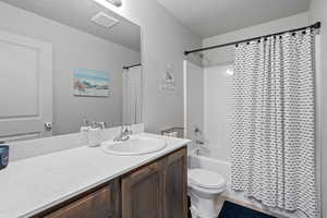 Full bathroom with toilet, vanity, shower / tub combo with curtain, and a textured ceiling