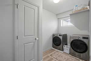 Laundry area with washing machine and dryer, a textured ceiling, and light wood-type flooring