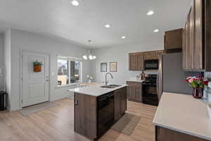 Kitchen with an island with sink, light wood-type flooring, hanging light fixtures, black appliances, and sink