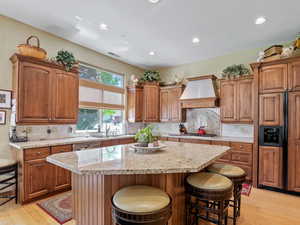 Kitchen with premium range hood, light stone countertops, a center island, and a kitchen breakfast bar