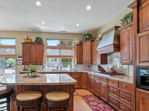 Kitchen featuring stainless steel gas stovetop, a center island, light stone counters, custom range hood, and light wood-type flooring