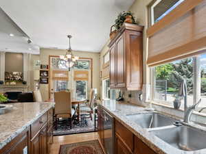 Kitchen with sink, an inviting chandelier, light hardwood / wood-style flooring, dishwasher, and light stone countertops