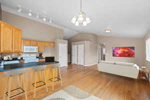 Kitchen featuring white appliances, hanging light fixtures, light hardwood / wood-style floors, vaulted ceiling, and a chandelier