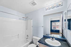 Full bathroom with vanity, toilet, a textured ceiling, and  shower combination