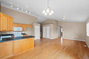 Kitchen with white appliances, decorative light fixtures, sink, and light wood-type flooring