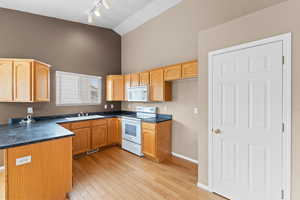 Kitchen with high vaulted ceiling, sink, light wood-type flooring, track lighting, and white appliances