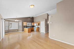 Kitchen featuring lofted ceiling, white appliances, a center island, decorative light fixtures, and light wood-type flooring