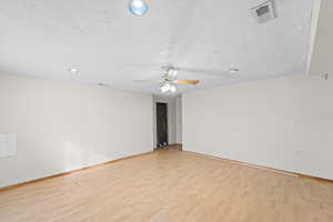 Unfurnished room with ceiling fan, a textured ceiling, and light wood-type flooring