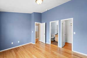 Unfurnished bedroom with vaulted ceiling, ensuite bathroom, a walk in closet, light hardwood / wood-style floors, and a closet