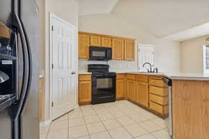 Kitchen with light tile patterned floors, sink, vaulted ceiling, black appliances, and kitchen peninsula