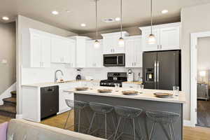 Kitchen with light hardwood / wood-style flooring, sink, appliances with stainless steel finishes, white cabinets, and pendant lighting