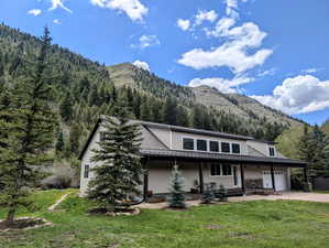 View of front of house featuring a mountain view, driveway, a front yard, a wooded view, and covered porch