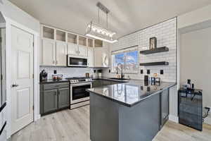 Kitchen with sink, gray cabinets, stainless steel range with gas stovetop, kitchen peninsula, and white cabinets