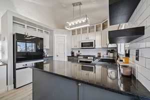 Kitchen featuring tasteful backsplash, white cabinets, decorative light fixtures, gas stove, and dark stone countertops