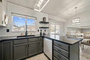 Kitchen with light wood-type flooring, stainless steel dishwasher, decorative light fixtures, sink, and kitchen peninsula