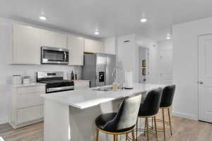 Kitchen with appliances with stainless steel finishes, sink, light hardwood / wood-style flooring, white cabinetry, and an island with sink