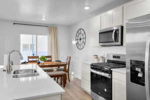 Kitchen with white cabinets, light hardwood / wood-style flooring, stainless steel appliances, and sink