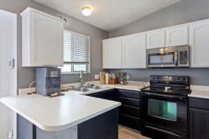 Kitchen with vaulted ceiling, sink, black range with electric cooktop, kitchen peninsula, and white cabinets