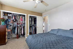 Bedroom with carpet, multiple closets, a textured ceiling, and ceiling fan