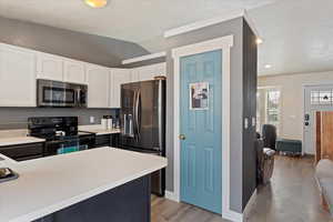 Kitchen with stainless steel appliances, a textured ceiling, white cabinets, lofted ceiling, and light wood-type flooring