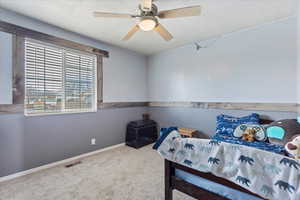 Bedroom with ceiling fan, carpet floors, and a textured ceiling