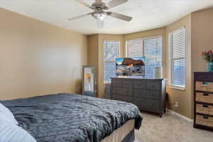 Bedroom with a textured ceiling, light carpet, and ceiling fan