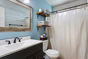 Bathroom with toilet, vanity, and curtained shower