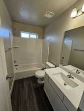 Full bathroom featuring washtub / shower combination, toilet, hardwood / wood-style floors, and a textured ceiling