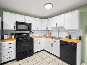 Kitchen with light tile patterned floors, sink, wooden counters, white cabinetry, and black appliances