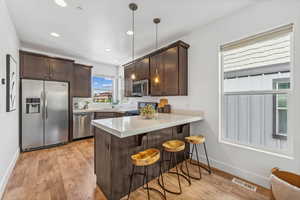 Kitchen with hanging light fixtures, a breakfast bar area, stainless steel appliances, light hardwood / wood-style floors, and kitchen peninsula