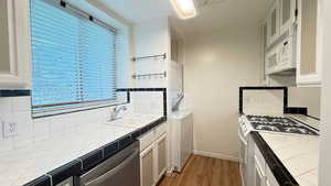 Kitchen featuring white appliances, white cabinets, tile counters, stacked washing maching and dryer, and sink