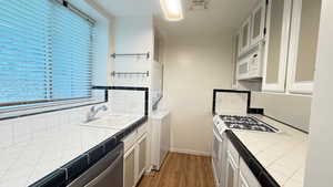 Kitchen featuring white appliances, stacked washer and clothes dryer, tile counters, sink, and white cabinetry