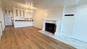 Unfurnished living room with a tiled fireplace, light hardwood / wood-style floors, and a notable chandelier