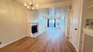 Unfurnished living room featuring light wood-type flooring, crown molding, a textured ceiling, and a notable chandelier