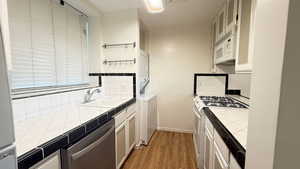 Kitchen featuring light wood-type flooring, tile countertops, sink, white appliances, and stacked washer and clothes dryer