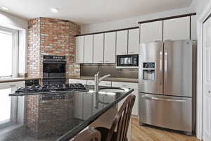 Kitchen featuring light hardwood / wood-style flooring, dark stone counters, black appliances, sink, and white cabinetry