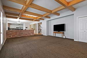 Unfurnished living room with coffered ceiling, a chandelier, beamed ceiling, and carpet flooring