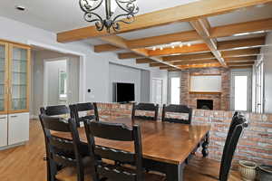 Dining room featuring a brick fireplace, a chandelier, light wood-type flooring, beamed ceiling, and french doors