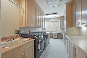 Clothes washing area featuring sink, cabinets, and washing machine and dryer