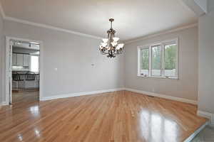 Empty room featuring a notable chandelier, crown molding, and light hardwood / wood-style floors