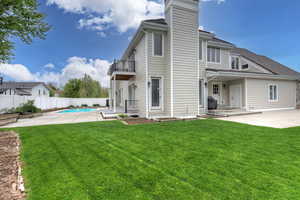 Back of property with a balcony, a lawn, a patio area, and a fenced in pool