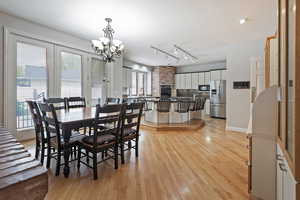 Dining area featuring rail lighting, light hardwood / wood-style flooring, an inviting chandelier, and a healthy amount of sunlight