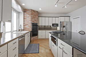 Kitchen featuring dark stone countertops, sink, light wood-type flooring, black appliances, and white cabinets