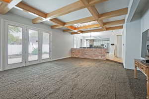 Unfurnished living room featuring coffered ceiling, carpet, a chandelier, and a healthy amount of sunlight