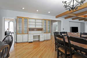 Dining room featuring light wood-type flooring, beamed ceiling, built in desk, and an inviting chandelier