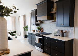 Kitchen with light wood-type flooring, decorative backsplash, stainless steel range with gas cooktop, and premium range hood